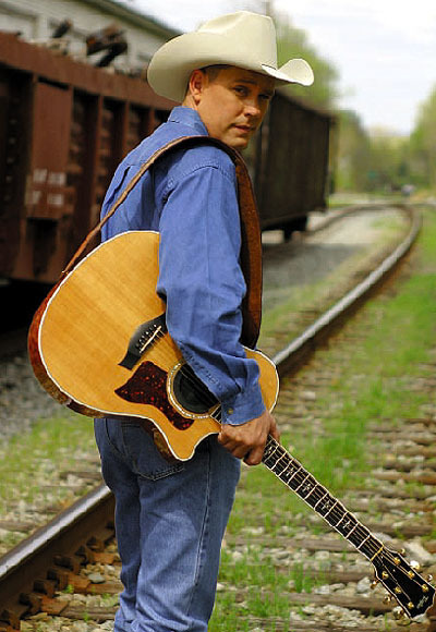 Pat waters in blue denim shirt standing with acoustic guitar